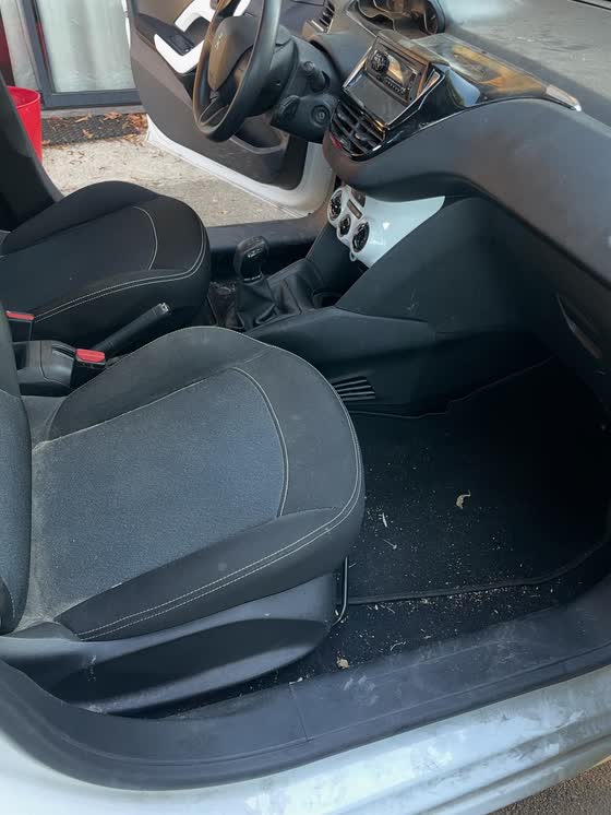 Intérieur d'une Peugeot 208 avant nettoyage : sièges poussiéreux et débris sur la moquette